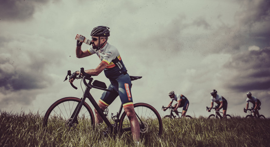 De Fietsende Vrienden zetten zich in voor de campagne Prikken tegen TBE met hun Tour Tegen TBE. Op de foto zie je 4 wielrenners. Robert Baarda staat stil i het hoge gras en drinkt water via een bidon. Op de achtergrond fietsen Richard Drenth, Age Yska en Arjan van Egmond voorbij.